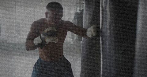 Shirtless backlit boxer training on heavy bag, punching with focus and strength