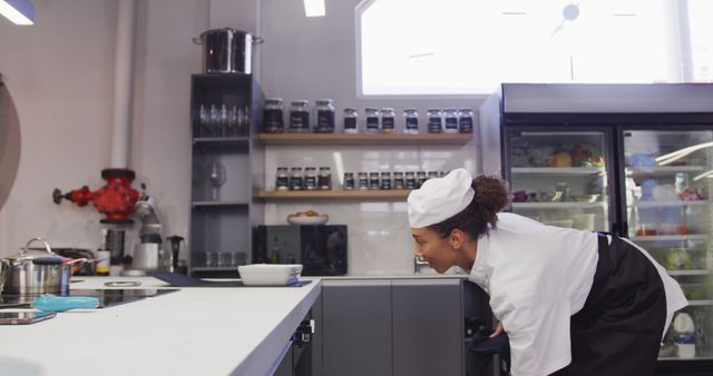 A professional chef prepares the kitchen in a restaurant backroom. The chef is wearing a traditional chef's hat and uniform, ensuring the kitchen is organized and ready for service. Cooking equipment and ingredients are visible in the background, highlighting a professional kitchen environment. This image is useful for culinary educational content, restaurant advertisements, cooking tutorial visuals, and food industry blogs.