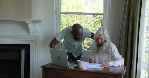 Elderly couple reviewing documents with laptop at home