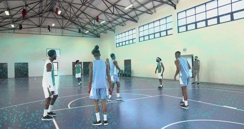 Indoor basketball team practicing defensive spacing drill on court under high ceiling