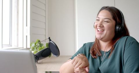 Happy biracial podcaster with headphones broadcasting from home