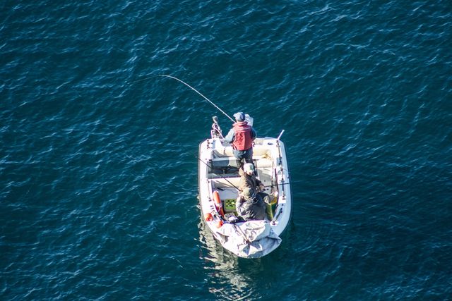 This stock image showcases two fishermen on a small boat fishing in the blue ocean. Captured from an aerial perspective, this shot highlights the vastness of the surrounding waters. Perfect for use in articles related to outdoor activities, fishing, hobbies, leisure, or relaxation. It can also be used in travel and tourism websites to promote boating or fishing tours.