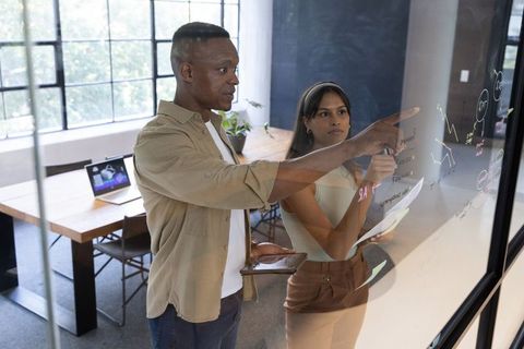 Diverse Coworkers Collaborate Using Glass Writing Board in Modern Office