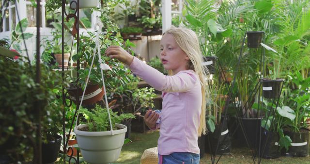 Caucasian girl touching plant with green leaves in flowerpot in garden. Childhood, nature, gardening and hobbies.