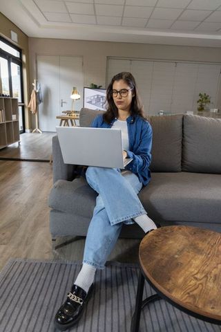 Asian woman working on laptop on modern sofa remote work lifestyle in bright living room