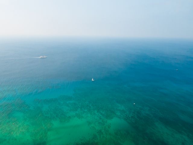 Aerial view of a sailboat and motorboat on a vast, calm ocean with clear blue water extending to the horizon. Ideal for illustrating themes of travel, maritime adventure, tranquility, or the beauty of aquatic sceneries. Suitable for use in travel blogs, maritime business advertisements, or ocean conservation campaigns.