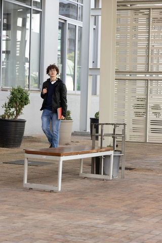 Teenage student walking through modern courtyard carrying red folder wearing headphones