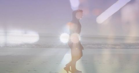 Silhouetted woman walking on wet shoreline with lens flare and ethereal backlit glow