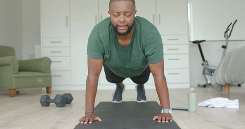 African american man holding plank on mat in minimalist bedroom home workout core strength