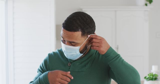 Man Adjusting Face Mask in Home Environment Wearing Green Sweater - Download Free Stock Images Pikwizard.com