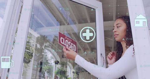 Small retail owner hanging closed sign on glass door with digital data overlays