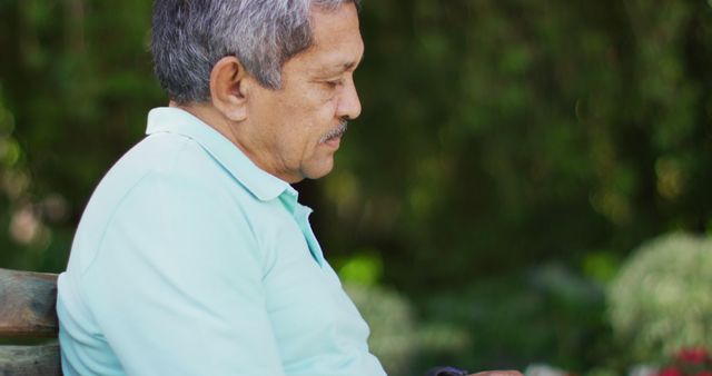 Senior man attentively reading his smartphone while sitting in garden with lush green surroundings. Great for illustrating senior citizens engaging with technology, outdoor relaxation, or aging and modern communication.