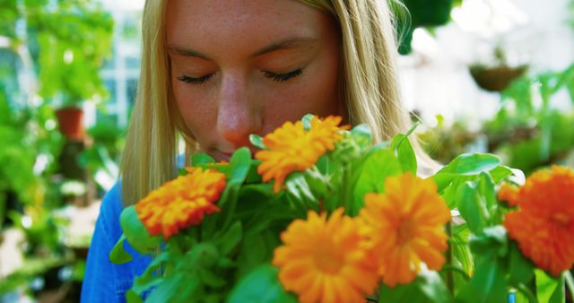 Young woman with blonde hair smelling vibrant orange marigold flowers surrounded by greenery. Ideal for promoting gardening, horticulture, botanical studies, relaxation, and nature-related content. Perfect for websites, blogs, and magazines focused on plants, wellness, and outdoor activities.