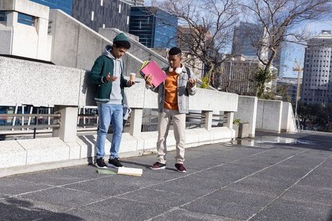 Teen students reacting to dropped notebooks on urban terrace with cityscape background