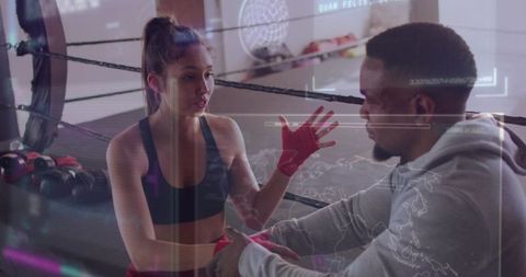 Female boxer receiving coach guidance and hand-wrap adjustment in futuristic boxing gym
