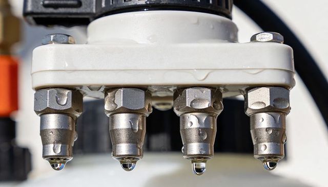Stainless nozzles dripping water from white manifold close-up with sunlit droplets