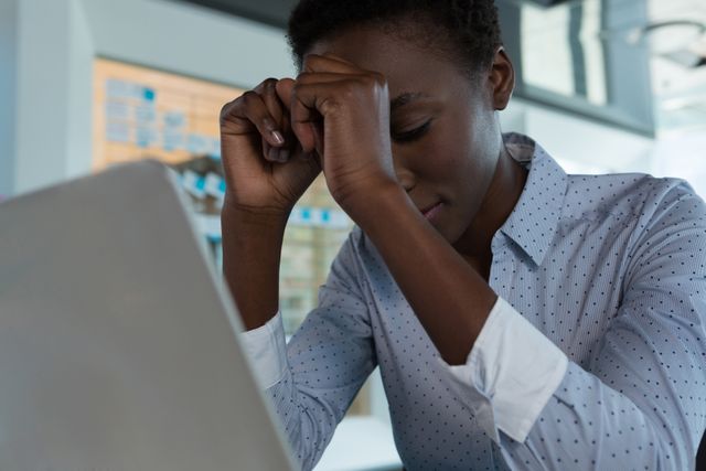 Businesswoman experiencing stress while working on a laptop in a modern office. Useful for illustrating workplace stress, mental health awareness, corporate environments, and professional challenges.