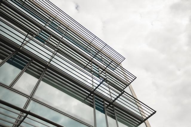 Image of a modern office building with a glass facade and steel structure, captured from a low angle against the sky. This image can be used for commercial real estate advertisements, business presentations, architectural portfolios, and urban development projects.