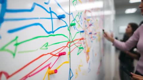 Women drawing colorful arrows on glass board during collaborative mapping workshop and brainstorming