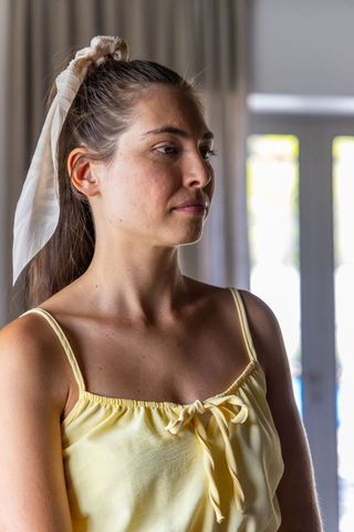 Serene young woman standing by window wearing yellow camisole and cream scarf