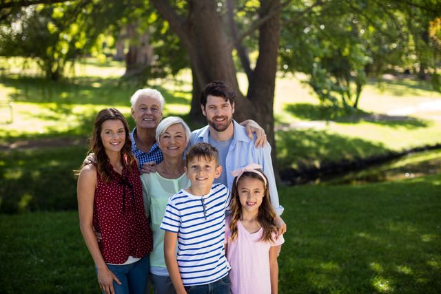 Multi-generation family standing together in a park, smiling and enjoying a sunny day. Ideal for use in advertisements, family-oriented content, lifestyle blogs, and promotional materials highlighting family values and outdoor activities.