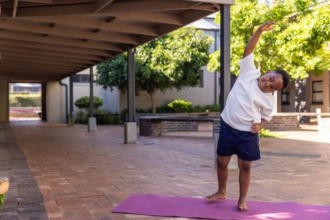 African american boy stretching on purple yoga mat in sunlit courtyard practicing fitness