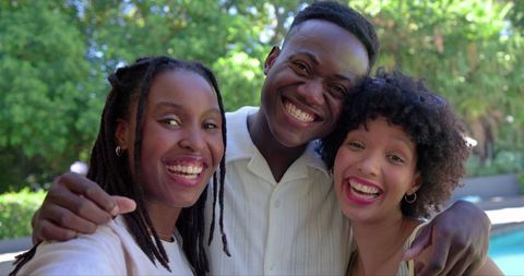 Smiling african american friends posing for selfie beside sunlit backyard pool
