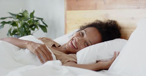 Smiling Woman Relaxing on Bed with Indoor Plant Ambiance