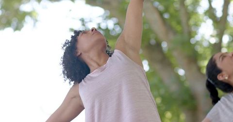 Multicultural women stretching under tree canopy practicing yoga and partner stretches