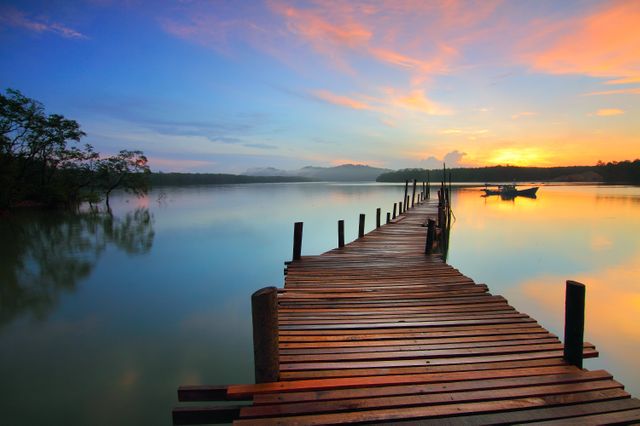 Perfect for travel brochures, relaxation-themed campaigns, and nature articles, this image captures a tranquil sunset over a wooden dock with calm waters. The boat in the distance adds a touch of maritime charm, and the vibrant colors in the sky enrich visual appeal.