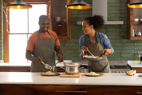Couple cooking and plating pasta together in bright farmhouse kitchen
