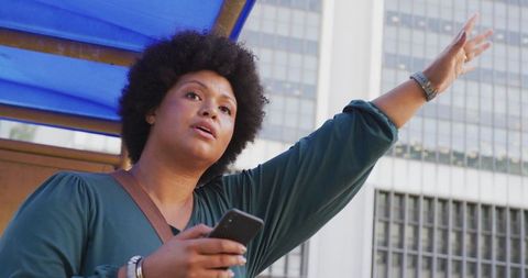 Woman Hailing Taxi in Urban Setting with Smartphone