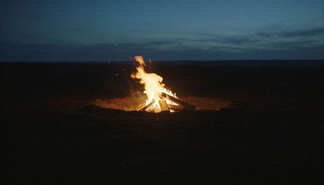 Lone bonfire burning on remote plain at twilight with rising embers and warm glow