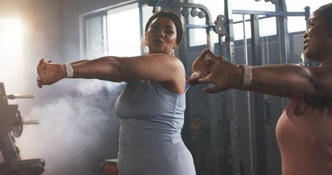Diverse women stretching arms across chest in gym during upbeat group workout session