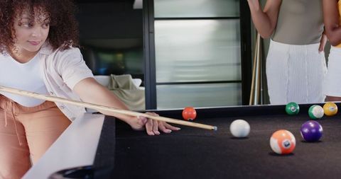 African american woman aiming cue on black-felt pool table during home billiards night