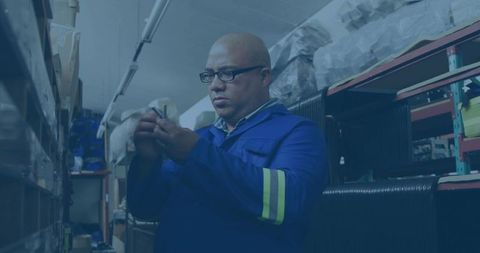 Warehouse worker inspecting component amid industrial shelving