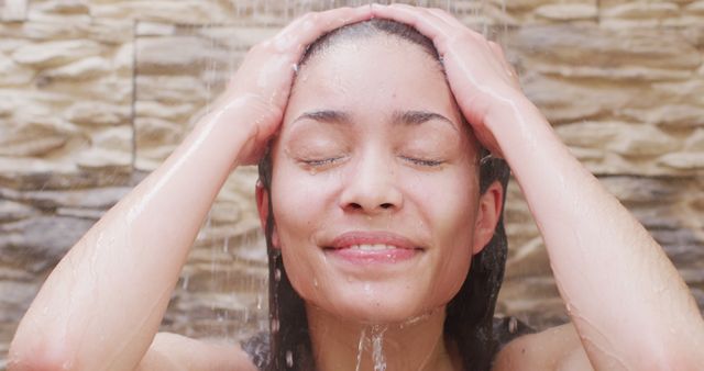 Woman enjoying a shower, water cascading down her face. Ideal for marketing wellness, beauty products, bath accessories, relaxation techniques, and hygiene campaigns. Perfect for blogs or articles focusing on self-care and health.