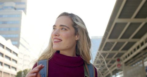 Young woman looking up while walking with backpack on sunlit urban walkway