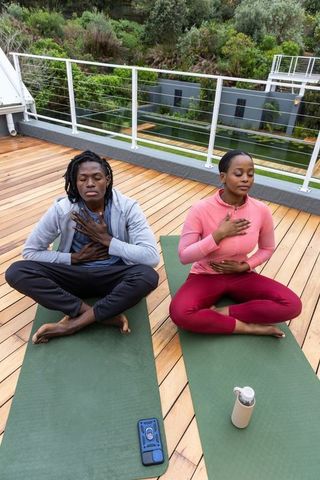 African american couple practicing mindful breathwork on rooftop deck with greenery