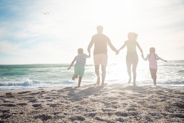 Family holding hands running towards ocean on sunny beach. Perfect for promoting family vacations, summer activities, outdoor fun, and lifestyle content. Ideal for travel brochures, family-oriented advertisements, and social media campaigns focused on togetherness and leisure.