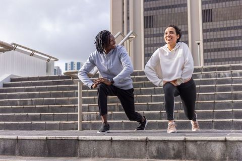 Diverse friends exercising outdoors doing lateral lunges on urban steps for city fitness