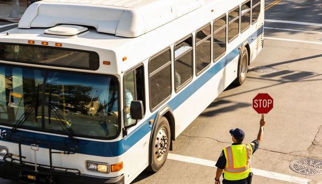 City bus stopping at intersection with crossing guard holding stop sign