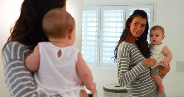 Mother holding her baby while both are looking into a mirror, conveying themes of bonding and mother-child connection. The family setting and smiles make it ideal for use in parenting blogs, family-oriented advertisements, and articles about motherhood and child development.