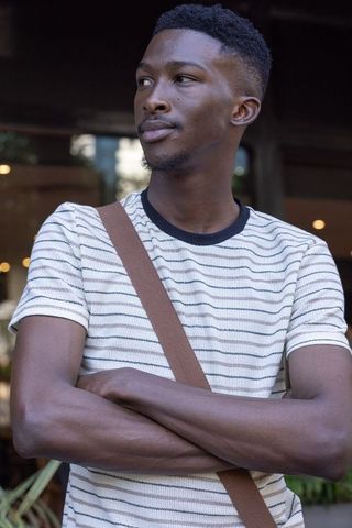 Confident african man standing with arms crossed wearing striped tee and crossbody bag