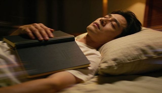 Serene man resting on bed at night with hardcover books on chest, warm cozy bedtime mood