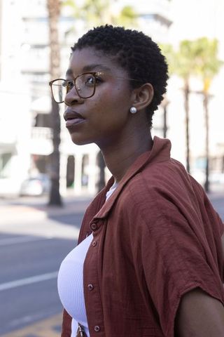African american woman wearing glasses and pearl earrings on sunlit city street
