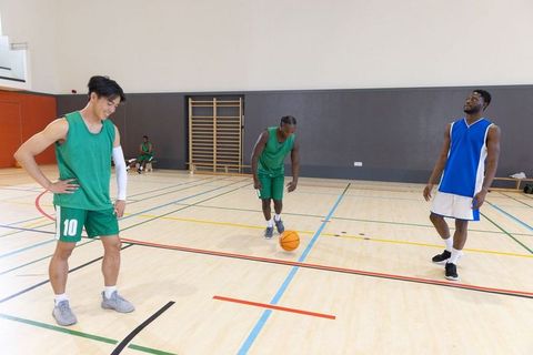 Practicing dribbling and teamwork on indoor basketball court with diverse players