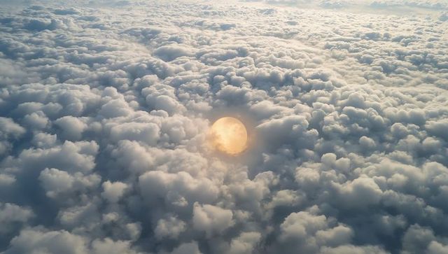 Rising glowing sunlike orb illuminating vast cumulus cloud sea with golden halo aerial panorama sunr