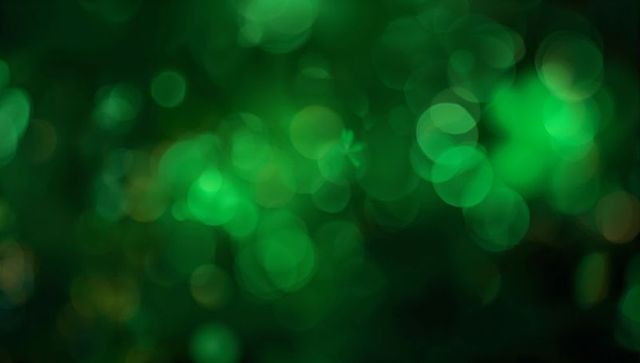 Glowing emerald bokeh orbs creating soft abstract green light background for design