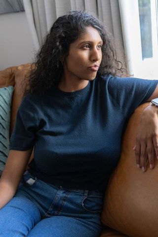 African american woman sitting on leather sofa gazing toward window in cozy sunlit room